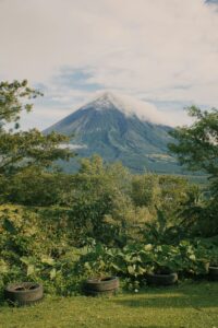 Scenic view of a volcano with lush vegetation in the foreground under a cloudy sky.